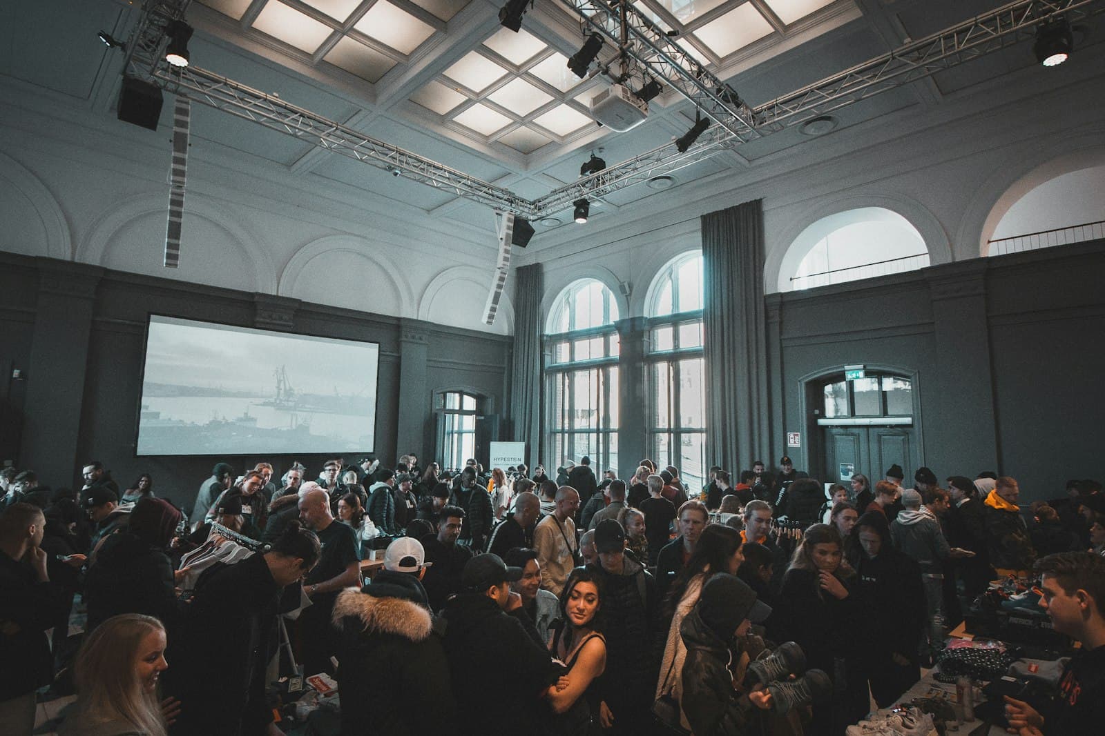 Veranstaltung in einem großen Saal mit Traversenkonstruktion, Leinwand und zahlreichen Gästen